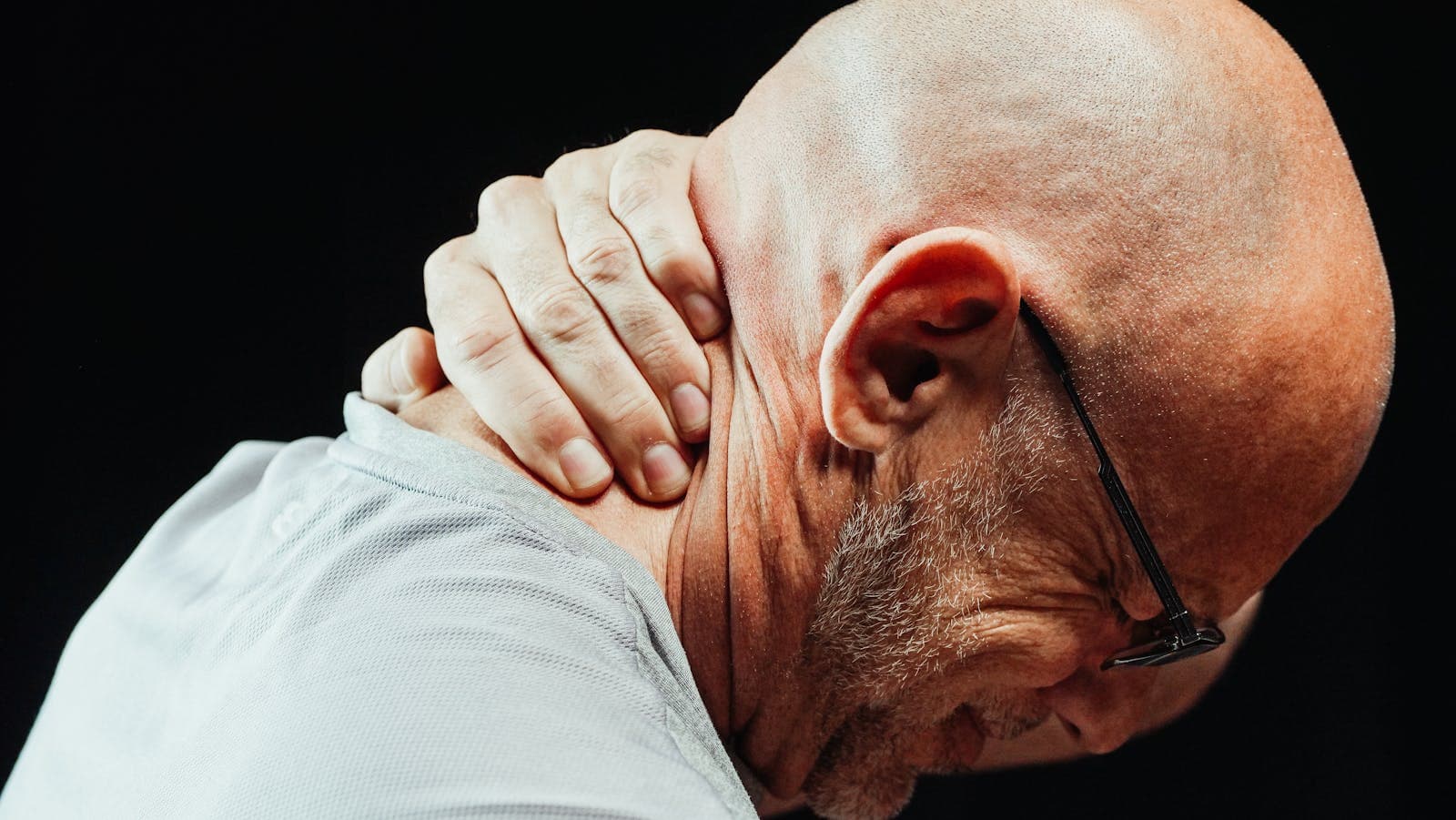 Homem com as mãos na região cervical demonstrando tensão muscular no pescoço